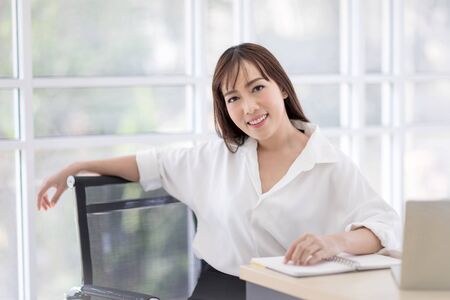 Beautiful Asian businesswomen wearing a white shirt sitting in the office, smiling confidently and looking at the camera. Asian business women, business owners, and office staff. Conceptの写真素材