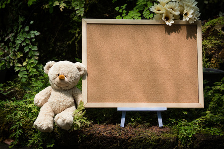 Brown teddy bear sitting near big blank board in the nature and sunlightの写真素材