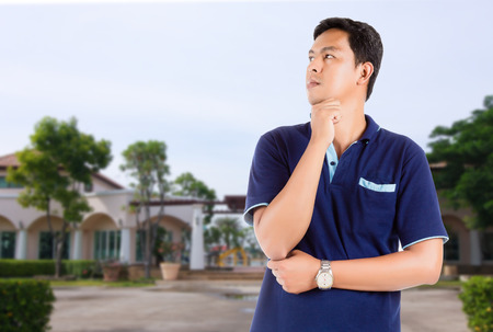 Portrait of young man wearing blue T-shirt in a contemplative pose on beautiful house background and include path, concept Planning to buy new propertyの写真素材