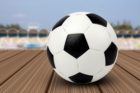 Black and white soccer ball on the wooden floor or plank with blurry soccer stadium backgroundの写真素材