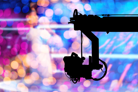 Abstract with silhouette of Television Camera hanging on crane is working on stage and blurry colorful light in studio concert backgroundの写真素材