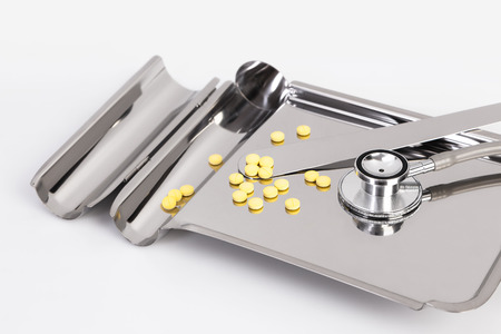 The yellow pills and stethoscope on Medication tray stainless on white backgroundの写真素材