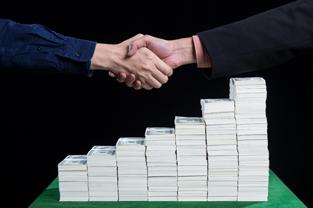 Two businessman shaking hand above the stack of dollars in increasing steps on black background concept business collaborationの写真素材