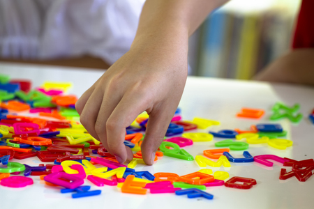 Selective focus at the hand is grabbing yellow in pile of colorful plastic letters on white tableの写真素材