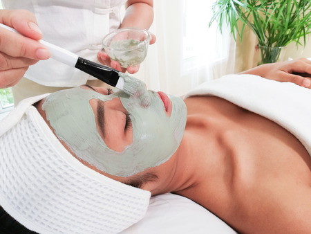 Young woman lay on white bed and get mask with green clay from specialists about facial, relax time and beauty of ladyの写真素材