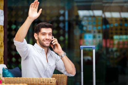 Young businessman sitting luggage and use smartphone to call in hotel corridor, copy spaceの写真素材