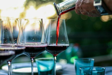 Man pouring red wine into glasses.