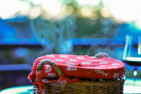 Wooden basket with hot food with steam rising and sunset in the background. Dinner served at home on...