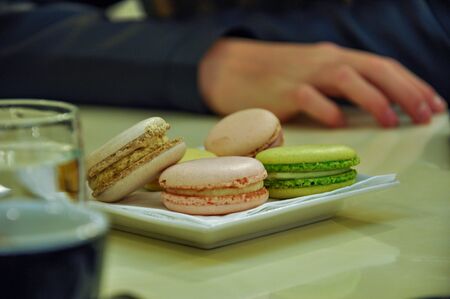 Detail of coloured french macaroons in Prague restaurant. Glass of water and cup in the background.