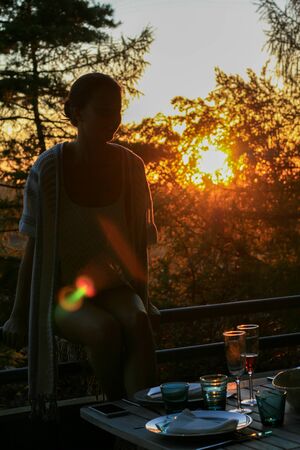Beautiful young woman girl sitting on terrace railing at home in summer during sunset, dinner, on...