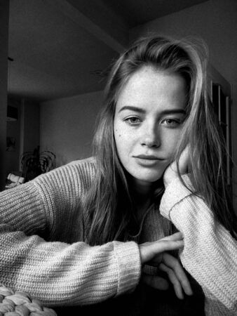 Portrait of beautiful young girl in sweater supporting her head with her hand, messy hair, chill...