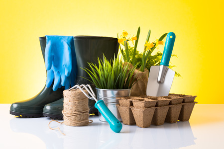 Garden equipment  boots, rake, shovel, pot, plant  over yellow backgroundの写真素材