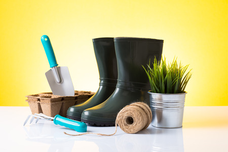 Garden equipment  boots, rake, shovel, pot, plant  over yellow backgroundの写真素材