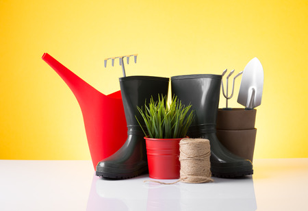 Garden equipment  boots, rake, shovel, pot, plant  over yellow backgroundの写真素材
