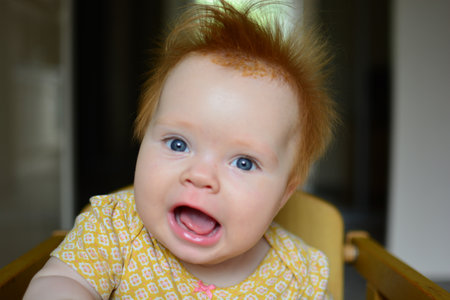 Baby girl sitting in a feeding chair and waiting for food with open mouth. Baby portrait with open...
