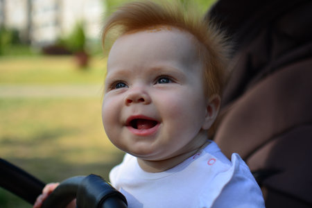 Cute baby girl sitting in a baby stroller and dreamy looking into the sky. Amused infant staring.