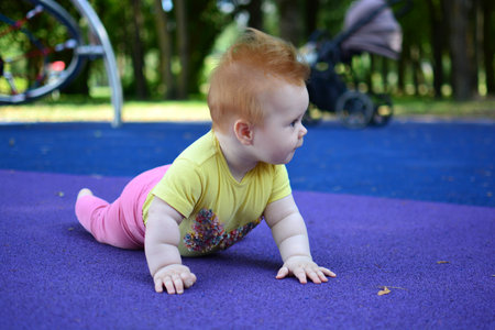 Red hair baby girl is crawling in children playground area in summer. Infant is spending time in playground.の写真素材