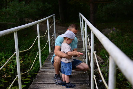 Father and son throwing rocks into water from small bridge. Father teaching son how to throw rock into pond.の写真素材
