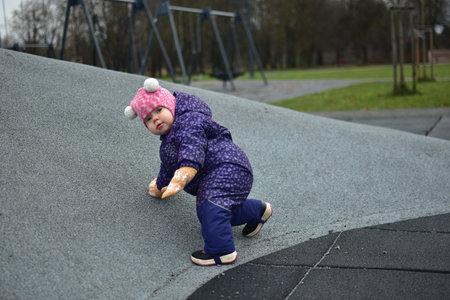 Baby girl playing in children playground in city park in cold weather autumn. Toddler girl having...