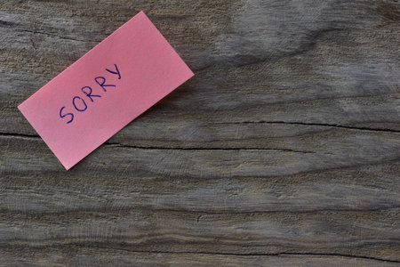 Message sorry on pink sticky note on wooden board textured background. A pen wrote word sorry on note paper.の写真素材