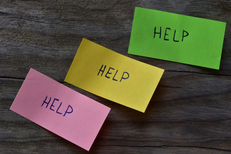 Message help on pink green and yellow sticky note on wooden board textured background. A pen wrote...
