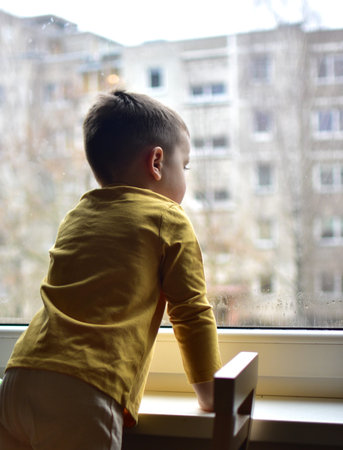 Toddler boy curiously looking through the window. Son impatiently waiting parents.の写真素材