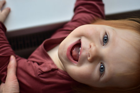 Red messy hair toddler girl curiously looking head up. Daughter impatiently waiting for attention. Kids face close up view from the top.の写真素材