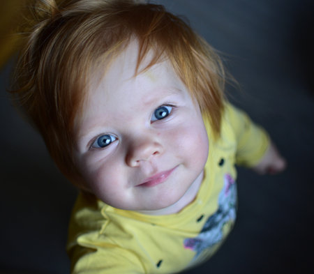 Red messy hair toddler girl curiously looking head up. Daughter impatiently waiting for attention. Kid view from the top.の写真素材