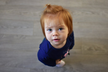 Red hair toddler girl curiously looking head up. Daughter impatiently waiting for attention. Kid portrait view from the top.の写真素材
