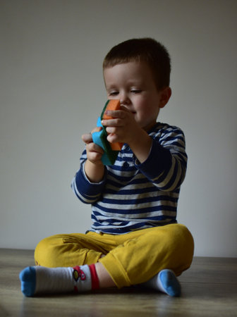 Toddler boy sitting crossed legs on table and playing with dish washing sponges. Kid playing with kitchen cleaning sponges at home.の写真素材