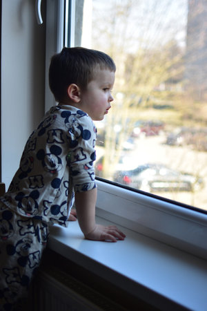 Toddler boy curiously looking through the window. Son waiting for parents.の写真素材