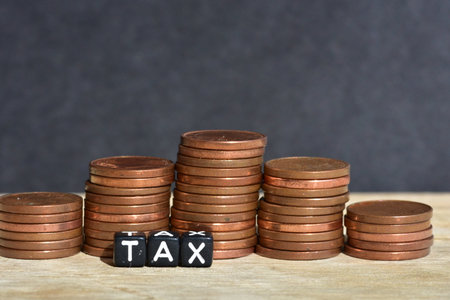 Stacked coins into five columns on wooden background and word tax made of plastic beads. concept of money economics tax idea copy spaceの写真素材
