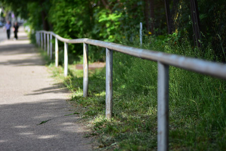 A perspective view of a weathered metal railing alongside a pedestrian pathway, surrounded by green grass and trees. Ideal urban safety infrastructure and outdoor barrier concept image.の写真素材