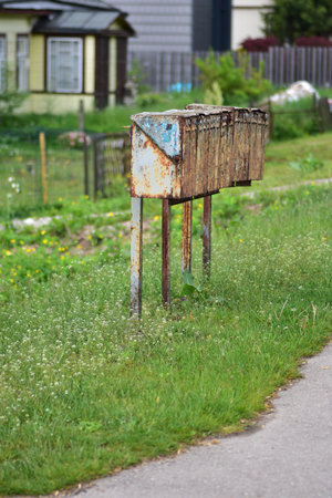Row of old, rusty metal mailboxes on a rural roadside. Weathered and vintage appearance, surrounded by grass and greenery. Represents abandonment, nostalgia, or rural communication systems.の写真素材