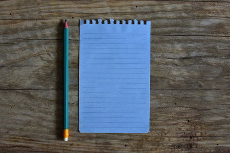 Blank note paper and a pencil on wooden background. Top view empty note book page on wooden table. Copy space simple minimal organizer concept.の写真素材