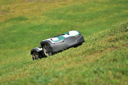 Autonomous robotic lawn mower working on a grassy hill. Smart garden technology for effortless lawn care. Eco-friendly, time-saving solution for modern landscaping and outdoor maintenance.の写真素材