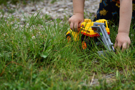 Young boy plays with yellow toy truck close up on grass. Candid outdoor moment showing creativity and exploration in nature. No face anonymous.の写真素材