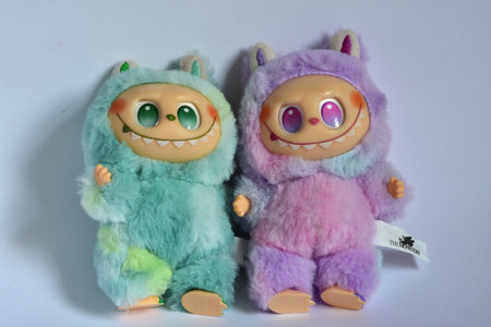 Two playful Labubu toy figures in a fluffy green and pink monster costumes and a mischievous smile, posed against a white background.のeditorial素材