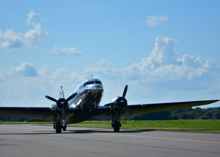 Shiny silver DC-3 vintage aircraft taxiing on runway, front view with twin propellers spinning,...