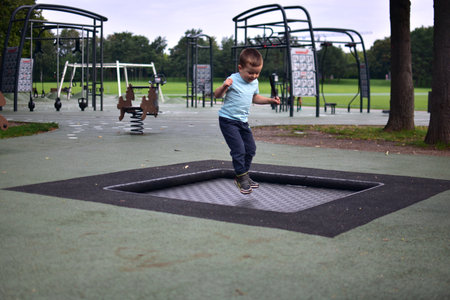 Toddler boy jumping on built-in playground trampoline, outdoor movement and energy moment in green park surroundings.の写真素材