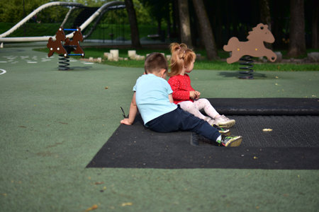 Two little children sitting together on trampoline border outdoors at playground, relaxing after active play, cute peaceful childhood moment in park nature environment.の写真素材