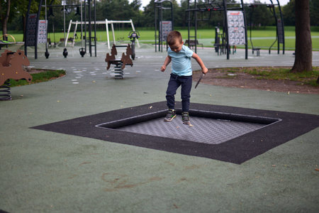 Toddler boy jumping on built-in playground trampoline, outdoor movement and energy moment in green park surroundings.の写真素材