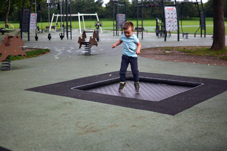 Toddler boy jumping on built-in playground trampoline, outdoor movement and energy moment in green park surroundings.の写真素材