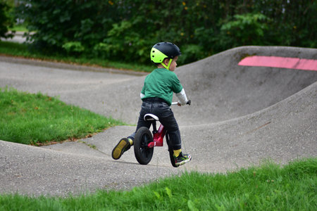 Toddler boy wearing helmet rides red balance bike on asphalt pump track. Active child learning balance and coordination while enjoying outdoor play in park.の写真素材