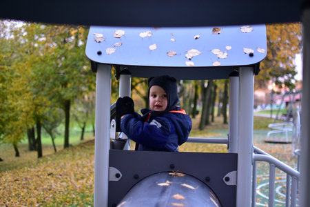 Happy little boy in blue snowsuit and hat playing in playground tower with telescope, smiling and...