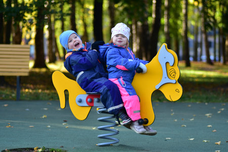 Two happy toddlers riding a colorful spring playground rocker in a city park. Joyful childhood...