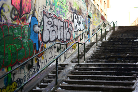 Long concrete stairway with metal railings and graffiti-covered walls. Urban winter scene with snow, strong leading lines, gritty city infrastructure, empty public space and street culture mood.のeditorial素材