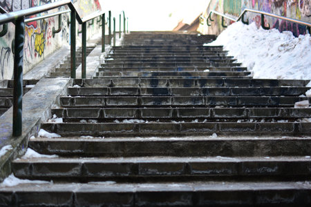 Concrete outdoor stairs covered with ice and snow, urban environment. Empty stairway with metal...