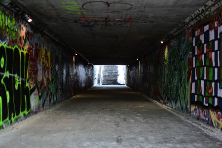 Empty underground pedestrian tunnel with graffiti walls and stairs leading outside. Urban winter scene, concrete passageway, moody lighting, city infrastructure and gritty street photography concept.のeditorial素材