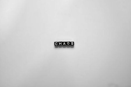 Word chaos spelled with black letter beads on white background. Minimalist concept of disorder,...